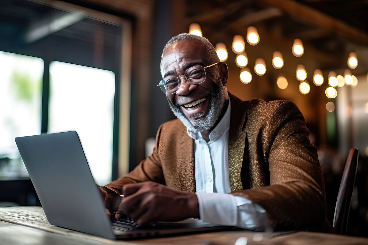 A smiling man reading from a laptop in a cafe